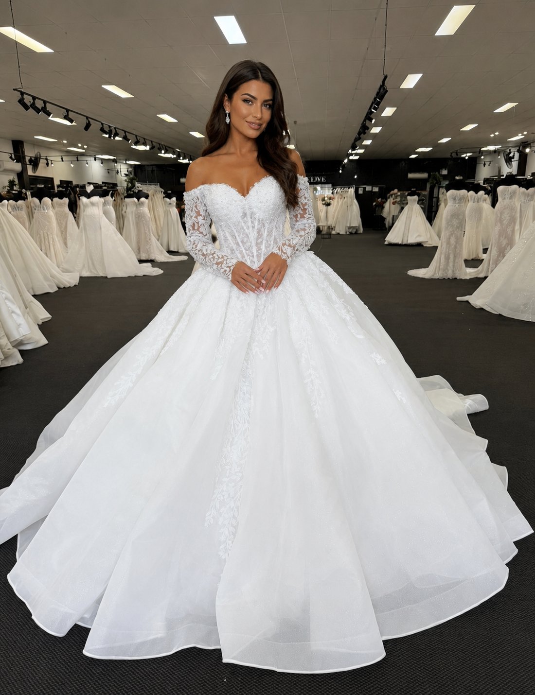 A bridal dream come to life ✨ This breathtaking off-the-shoulder ball gown features a sculpted corset bodice with intricate lace appliqué, sheer long sleeves, and a romantic sweetheart neckline. The voluminous glitter tulle skirt flows into a dramatic train, creating a regal silhouette made for unforgettable moments. Elegant, timeless, and utterly enchanting. 🤍