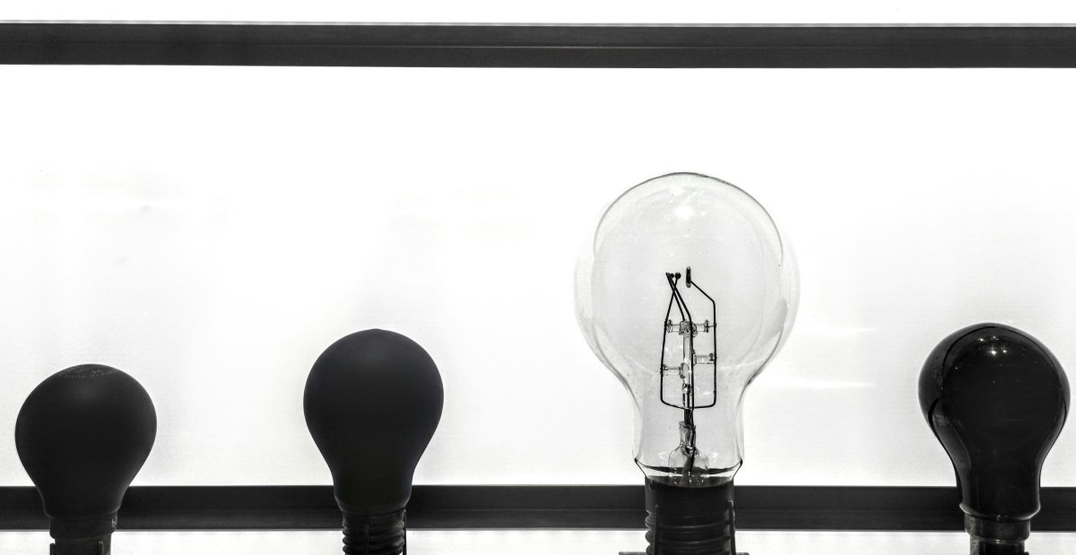 A row of four lightbulbs three of which are dark and unlit and one is clear and unlit