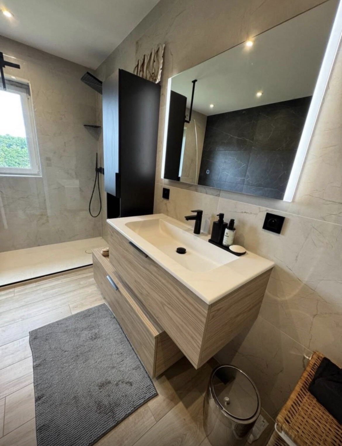 Salle de bains avec douche vitrée, meuble vasque en bois et grand miroir.